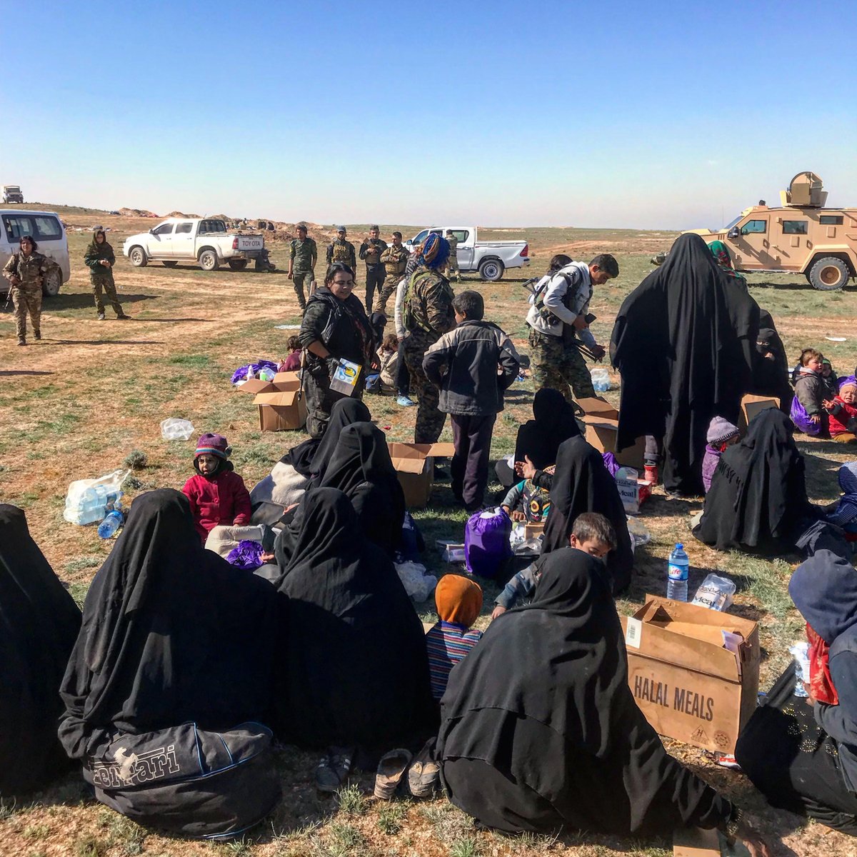 SDF evacuate IDPs/ISIS families from Baghuz. Off camera, US SOF hand out water, nappies and MREs and screen men separately, looking for fleeing ISIS fighters.   