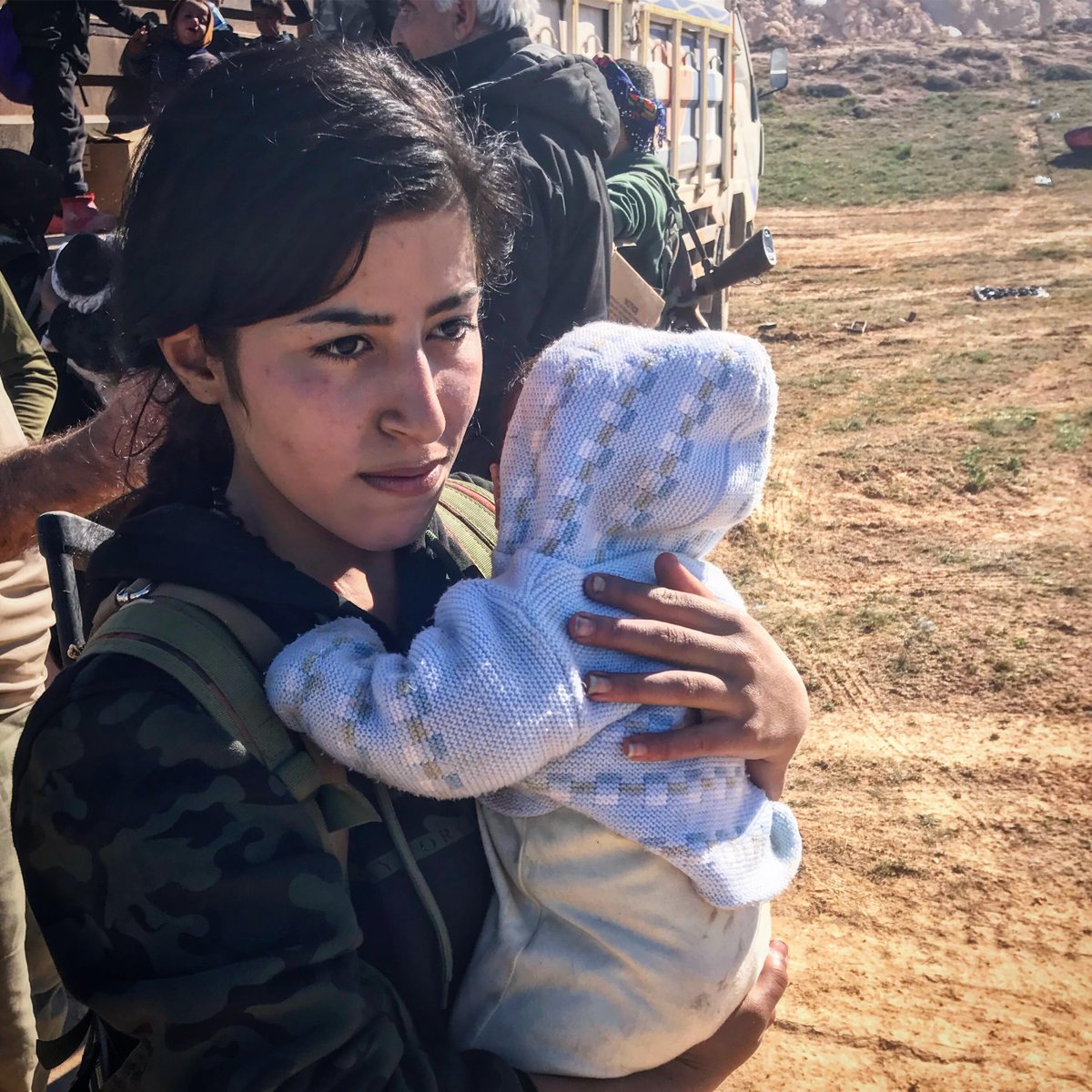 SDF evacuate IDPs/ISIS families from Baghuz. Off camera, US SOF hand out water, nappies and MREs and screen men separately, looking for fleeing ISIS fighters.   